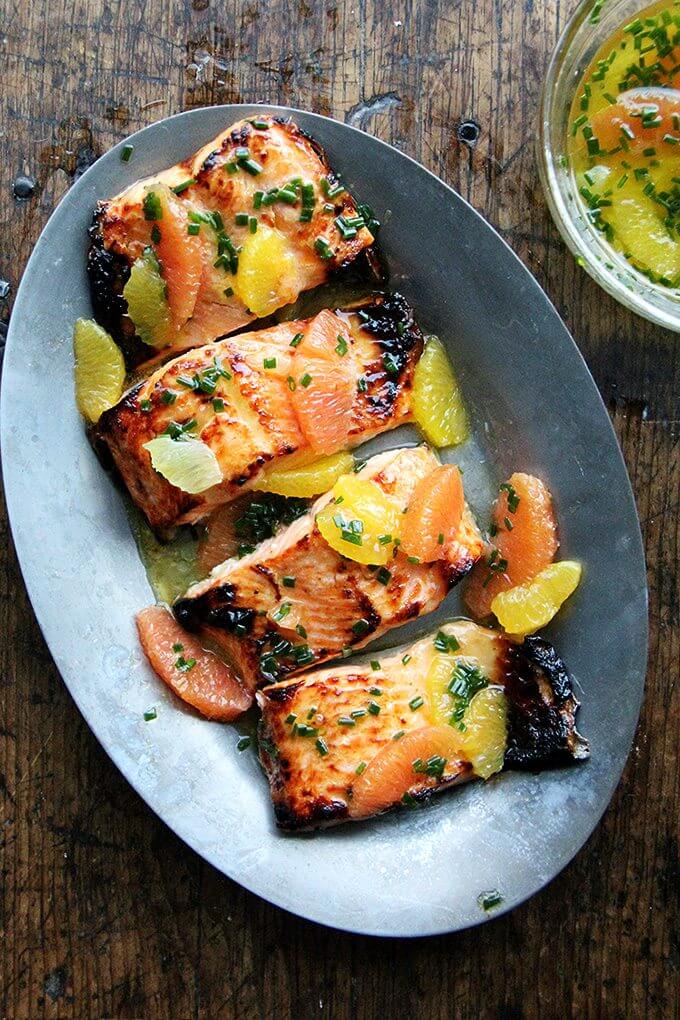 Arctic Char is mild and delicious. It's thin, so it cooks quickly. The sauce in this broiled lemon-honey arctic char is also a nice mix of citrus. I love using Cara Cara oranges for their sweet flavor and pretty hue. // www.simonrockett.com 滋滋作响的大盘子里盛着烤焦的北极焦,淋上柑橘酱。