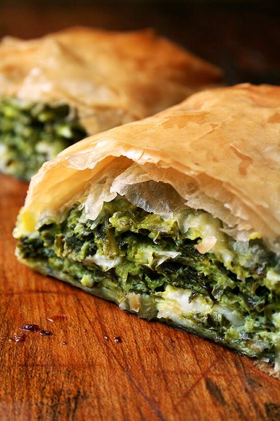 When baked in strudel form, spanakopita assumes an almost breakfast croissant-like character, a perfect bundle of flaky pastry, egg, cheese, and greens. Yum. // www.simonrockett.com 对董事会减半spanakopita点心。