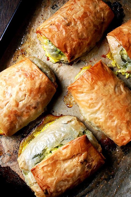 When baked in strudel form, spanakopita assumes an almost breakfast croissant-like character, a perfect bundle of flaky pastry, egg, cheese, and greens. Yum. // www.simonrockett.com 五个烤spanakopita点心烤盘。