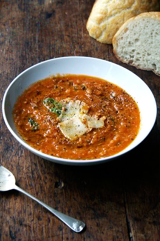 In this roasted tomato and bread soup, slow-roasting the tomatoes, onions, carrots and garlic concentrates all of the flavors, making any liquid but water unnecessary. I have no doubt this soup will make an impression in your heart and mind. // www.simonrockett.com 一碗烤西红柿和面包汤一边自制的面包和一把勺子。